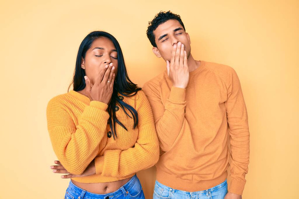 Beautiful latin young couple wearing casual clothes together bored yawning tired covering mouth with hand. restless and sleepiness.  - Foto, Imagen
