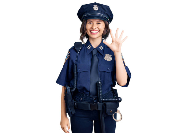 Молода красива дівчина в поліцейській формі показує і вказує пальцями номер п'ять, посміхаючись впевнено і щасливо
.  - Фото, зображення