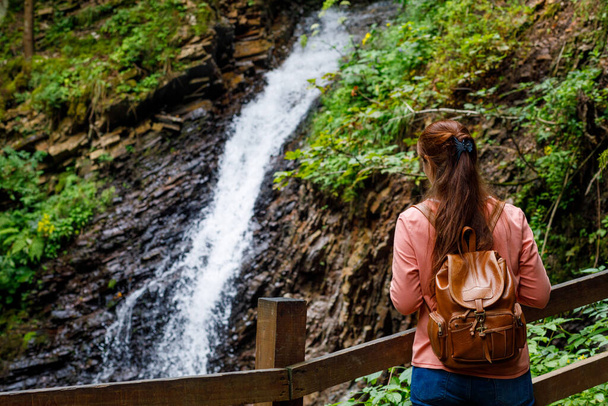 Woman tourist stands with a backpack on the background of a waterfall. - Foto, Imagem