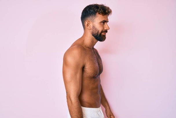 Junger hispanischer Mann, der ohne Hemd zur Seite schaut, entspannte Profil-Pose mit natürlichem Gesicht und selbstbewusstem Lächeln.  - Foto, Bild