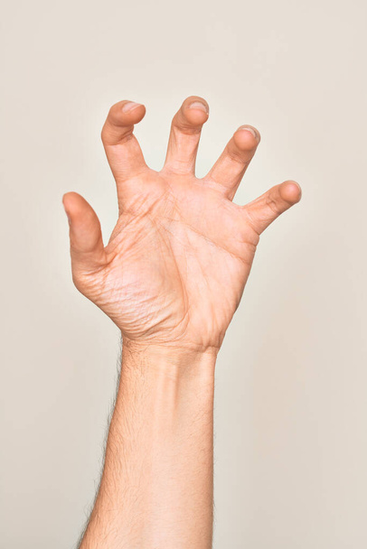 Hand of caucasian young man showing fingers over isolated white background grasping aggressive and scary with fingers, violence and frustration - Photo, Image