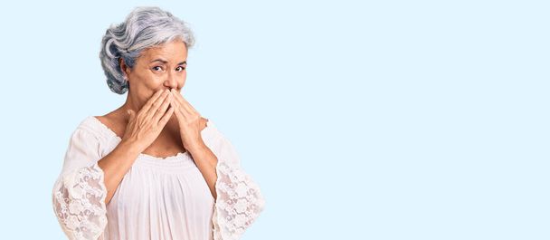 Ηλικιωμένη γυναίκα με γκρίζα μαλλιά που φοράει μποέμικο στυλ γελώντας και ντροπιασμένη χαχανίζοντας καλύπτοντας το στόμα με χέρια, κουτσομπολιά και σκάνδαλα  - Φωτογραφία, εικόνα