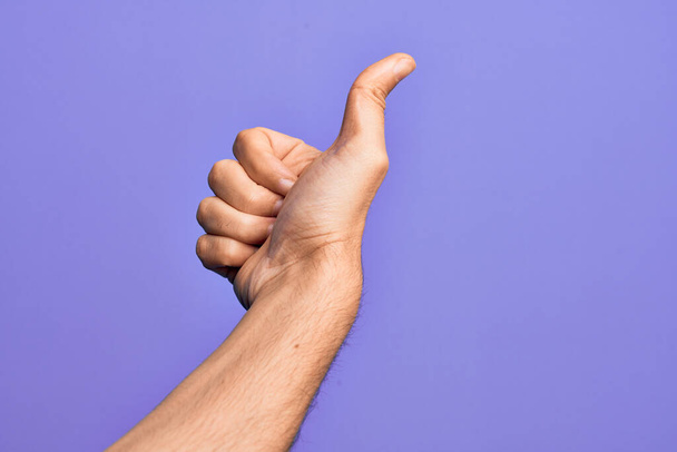 Hand of caucasian young man showing fingers over isolated purple background doing successful approval gesture with thumbs up, validation and positive symbol - Fotoğraf, Görsel