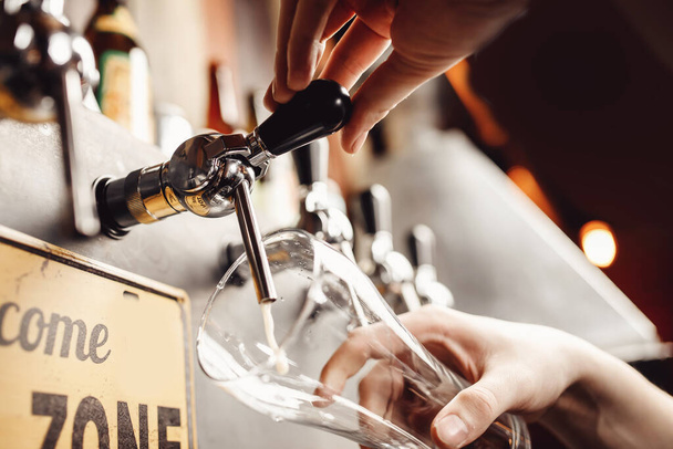 バーテンダーはビールをグラスに注ぎ込み、暗い背景にします。アルコールクラフトドリンクのコンセプト - 写真・画像