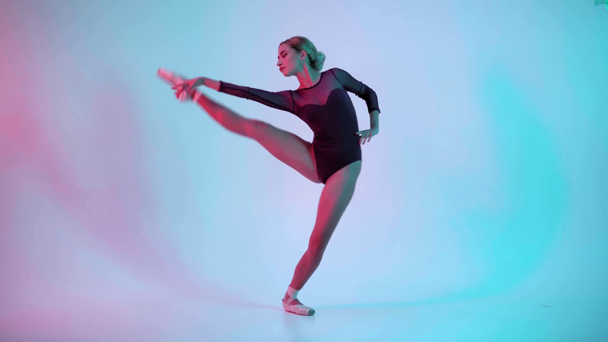 Fiatal balerina bemutató balett mozog kék és rózsaszín háttér - Felvétel, videó