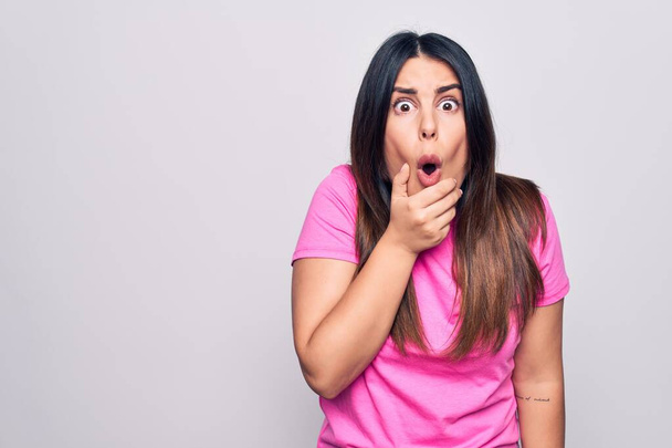 Young beautiful brunette woman wearing casual pink t-shirt standing over white background Looking fascinated with disbelief, surprise and amazed expression with hands on chin - Foto, afbeelding