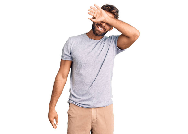 Jonge Spaanse man in casual kleding die ogen bedekt met een glimlachende arm vrolijk en grappig. blind concept.  - Foto, afbeelding