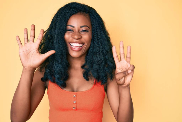 Belle femme africaine portant des vêtements décontractés montrant et pointant vers le haut avec les doigts numéro huit tout en souriant confiant et heureux.  - Photo, image