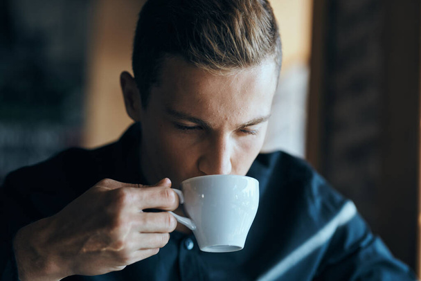 Geschäftsmann mit einer Tasse Kaffee in einem Café und einem dunklen Hemd hübsches Gesicht - Foto, Bild