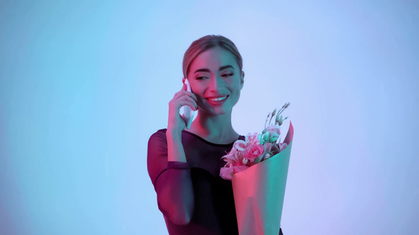 Молодая балерина с цветами разговаривает на смартфоне на синем и розовом фоне - Кадры, видео