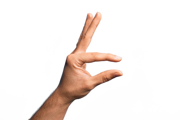 Hand of caucasian young man showing fingers over isolated white background picking and taking invisible thing, holding object with fingers showing space - Foto, Imagem