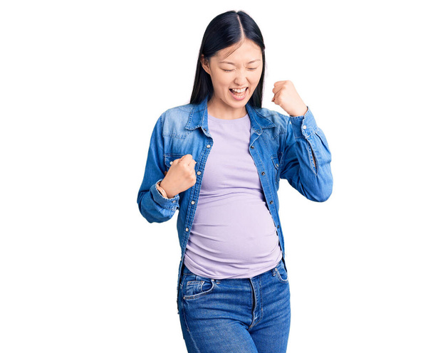 Молодая красивая китаянка беременна ожидая ребенка празднуя удивлен и поражен успехом с поднятыми руками и закрытыми глазами. победитель концепция.  - Фото, изображение