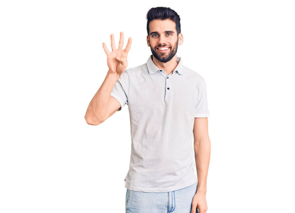 Joven hombre guapo con barba usando polo casual mostrando y apuntando hacia arriba con los dedos número cuatro mientras sonríe confiado y feliz.  - Foto, Imagen