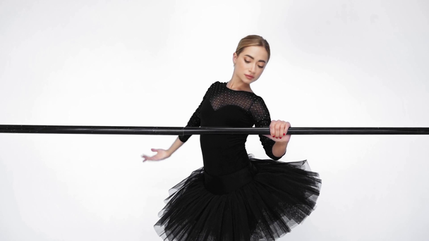 Elegante bailarina sosteniendo la barra y levantando la pierna sobre fondo blanco - Imágenes, Vídeo