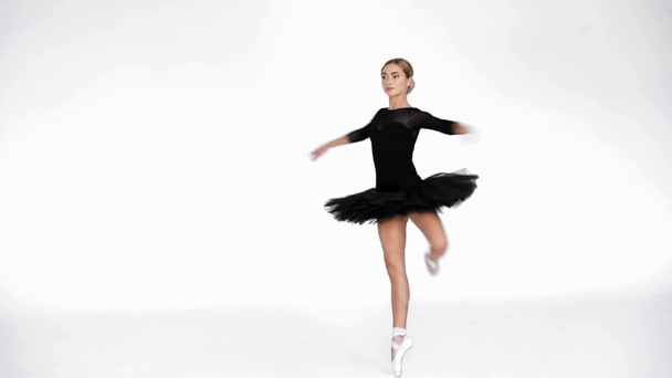 Молодая балерина в черной балетной юбке крутится и танцует на белом фоне - Кадры, видео
