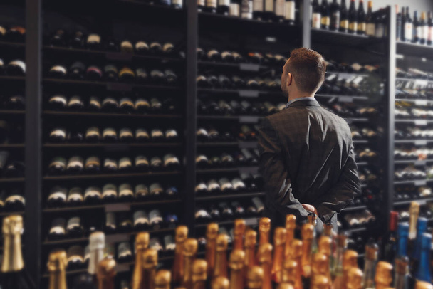 Sommelier Barmeni içki dükkanının yanındaki şarap şişesini seçiyor. - Fotoğraf, Görsel