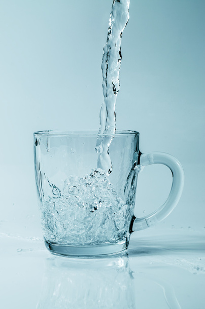 Agua que se vierte en una taza transparente sobre un fondo degradado
 - Foto, imagen