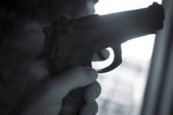Πιστόλι αυτόματο όπλο χειρός σε σιλουέτα στο χέρι του δολοφόνου ατμοσφαιρική σκοτεινή δραματική φωτογραφία. - Φωτογραφία, εικόνα