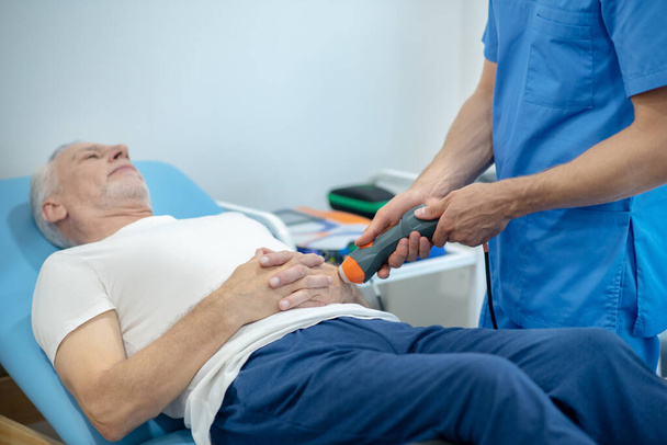 Gray-haired male patient lying on coach, receiving ultrasound hand treatment - Fotoğraf, Görsel