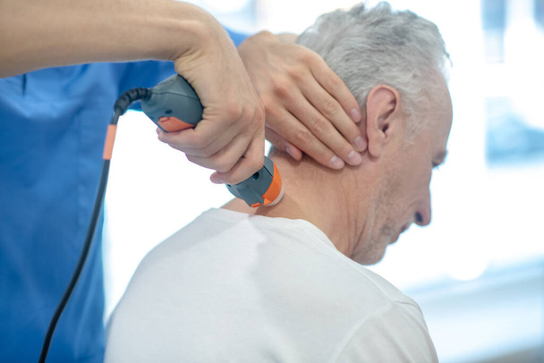 Back view of gray-haired male patient receiving ultrasound neck treatment - 写真・画像