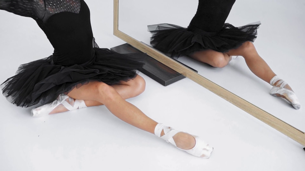 Elegante bailarina sentada y estirándose cerca del espejo sobre fondo blanco - Imágenes, Vídeo