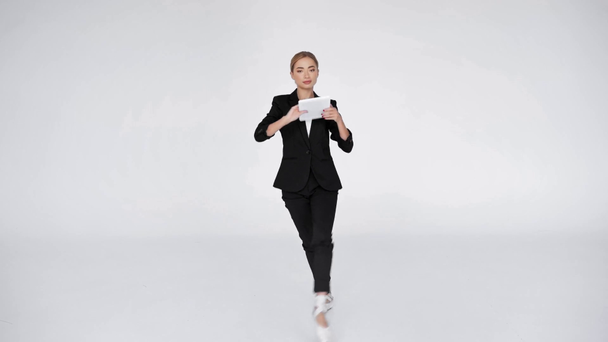 Κομψή μπαλαρίνα στο σημείο που δείχνει ψηφιακή ταμπλέτα στην κάμερα σε λευκό φόντο - Πλάνα, βίντεο