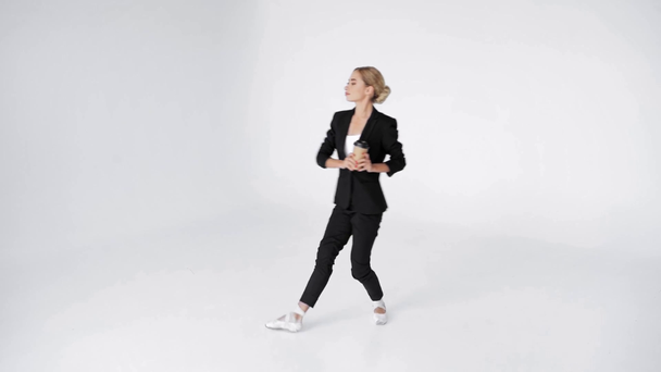 Bailarina joven caminando en punta con taza de papel de café sobre fondo blanco - Imágenes, Vídeo