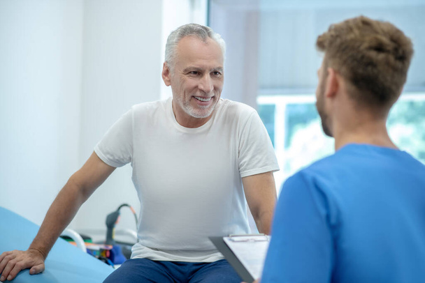 Achteraanzicht van bruinharige arts in gesprek met volwassen mannelijke patiënt - Foto, afbeelding