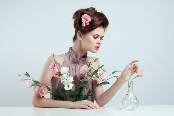 femme romantique avec des fleurs dans ses cheveux et vase avec une fleur rose table de fond clair - Photo, image