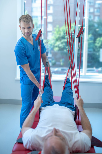 Male rehabilitation therapist helping to raise patients legs - Foto, immagini