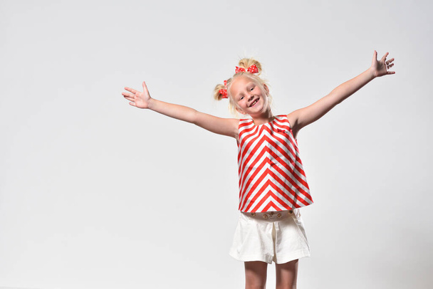 Blonde girl 7 years old smiles and opened her arms wide, studio photography - Foto, afbeelding