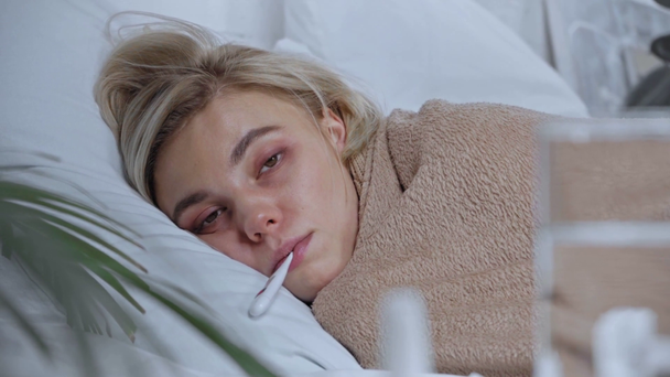selektywne skupienie chorej kobiety z cyfrowym termometrem w ustach leżącej na łóżku - Materiał filmowy, wideo