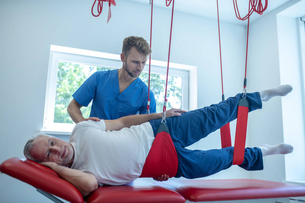 Young bearded doctor helping elderly patient to exercise - Foto, Bild
