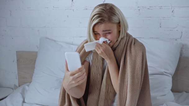 άρρωστη γυναίκα που έχει βιντεοκλήση στο smartphone και φτάρνισμα σε χαρτοπετσέτα - Πλάνα, βίντεο