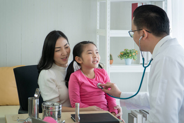Šťastná asijská, dospělá matka a dcera z dětství, prohlídka na klinice. pediatričku, poslouchej tlukot srdce školaček. Mužský lékař, konzultace a poradenství dětských pacientů - Fotografie, Obrázek