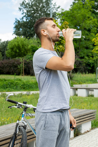 The man drinks water and listens to music with headphones. - Valokuva, kuva