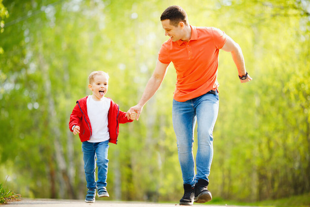 Ojciec i syn biegną po drogach w letnim parku. Szczęśliwa koncepcja rodziny - Zdjęcie, obraz