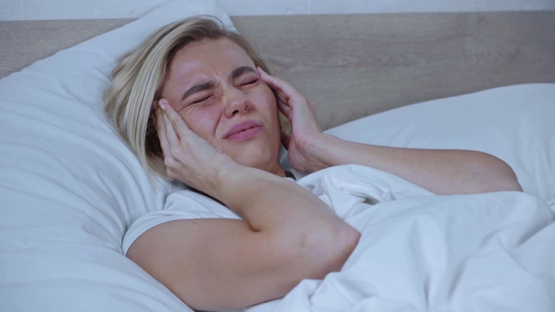 vermoeide vrouw met migraine die tempels aanraakt terwijl ze in bed ligt - Video
