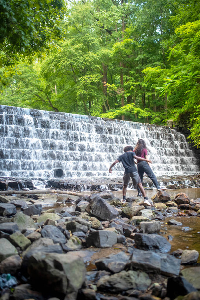 Двое молодых людей пересекают ступеньки у основания водопада. - Фото, изображение