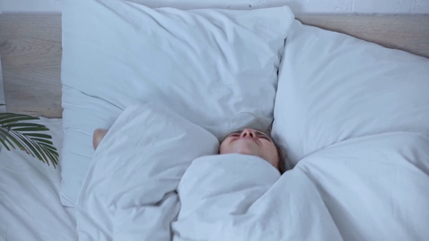 δυσαρεστημένη γυναίκα ξαπλωμένη κάτω από κουβέρτα και καλύπτοντας τα αυτιά στο κρεβάτι - Πλάνα, βίντεο
