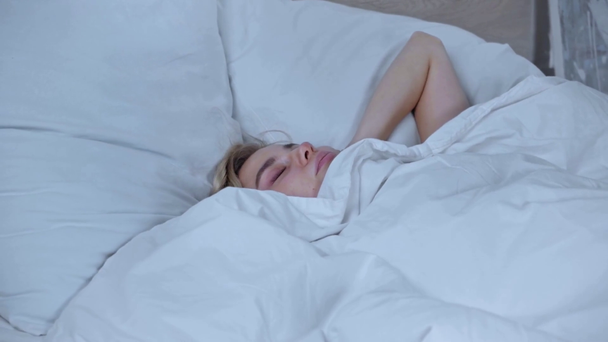 niezadowolona kobieta zakrywająca uszy leżąc pod kocem w łóżku - Materiał filmowy, wideo