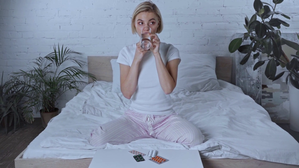 хвора жінка п'є воду, приймаючи таблетки біля блістерних пакетів у спальні
 - Кадри, відео