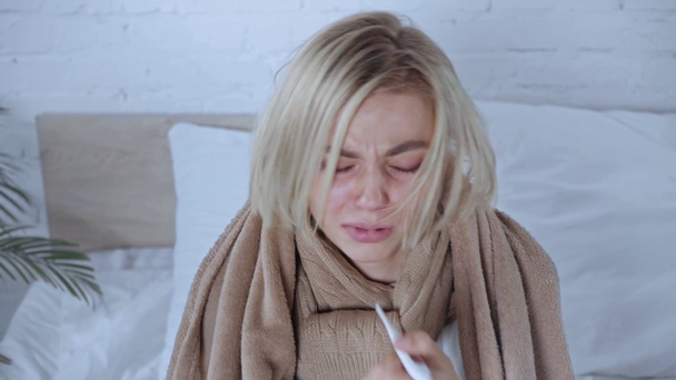άρρωστη γυναίκα τυλιγμένη σε κουβέρτα φτάρνισμα σε χαρτοπετσέτα και μέτρηση της θερμοκρασίας - Πλάνα, βίντεο