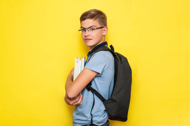 Uczeń nastolatka w okularach i szkolny plecak uśmiecha się na żółtym tle. Wracamy do szkoły.. - Zdjęcie, obraz