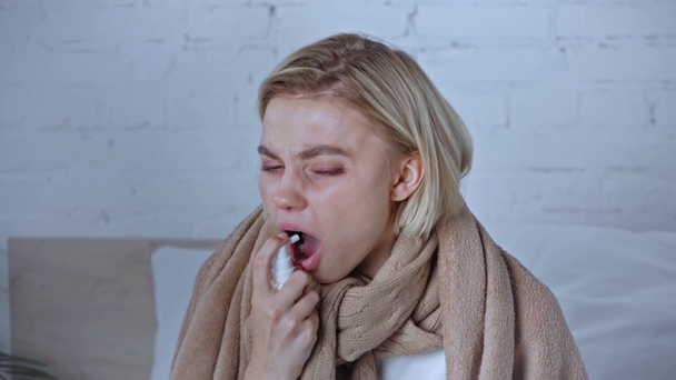 毛布に包まれた病気の女性は咳をしながら家で治療スプレーを使い - 映像、動画