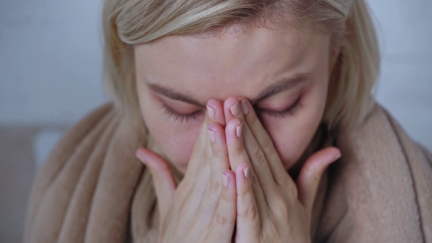 κοντινό πλάνο μιας άρρωστης ξανθιάς γυναίκας τυλιγμένης σε κουβέρτα αγγίζοντας το πρόσωπο - Πλάνα, βίντεο