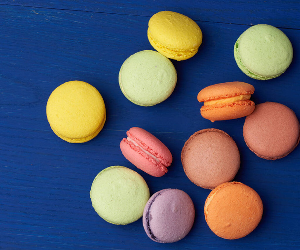 stack of multi-colored round baked macarons cakes on a blue wooden background, close up - Foto, afbeelding