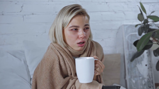 zieke jonge vrouw met kopje thee en afstandsbediening  - Video