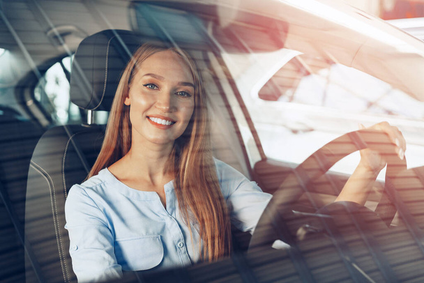 Attractive young woman sitting in new car in showroom - Foto, afbeelding