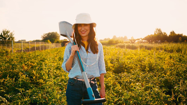 Женщина в шляпе держит лопату и стоит в поле  - Кадры, видео